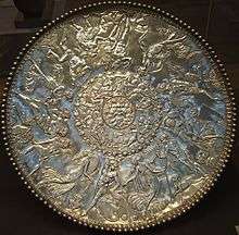 A large silver dish, decorated in bas relief in three rings. In the center ring, whose diameter is roughly 1/7 of the whole dish, is the face of a full-bearded man, with four bird heads pointing outwards along the diagonals. Around the second ring, frolicking sea creatures such as nereids are depicted; this ring's diameter is roughly 3/7 of the dish. Around the outermost ring, humans and a faun are depicted as dancing, making music, drinking and enjoying other pastimes.
