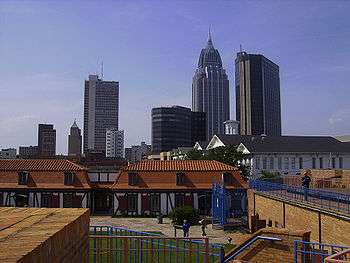 Skyline of a city, showing many tall buildings of varying heights in the background; A cluster of low-rise buildings and a small park are visible in the foreground.