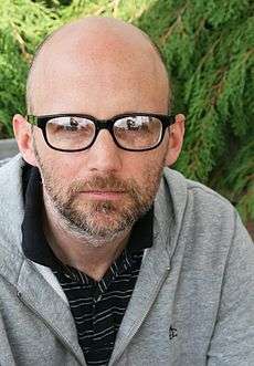 A bald man with glasses is looking intently at a camera.
