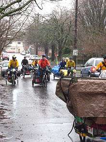 Cyclists pull covered trailers in the rain
