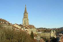 A grey stone Gothic spire rises above the Old City of Bern