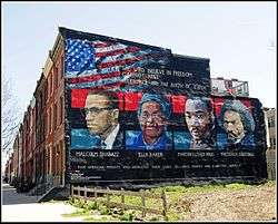 A painted mural shows the faces of Malcolm X, Ella Baker, Martin Luther King, and Frederick Douglass