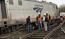 Four investigators look at one of the damaged train cars with Amtrak marked on the side
