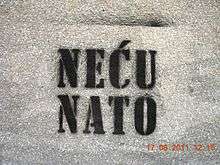 A white wall with black spray painted words "Neću Nato" on it.