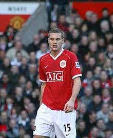 Nemanja Vidić, wearing a red Manchester United jersey with the AIG sponsor logo at the front centre and shorts with a number 15 and Nike logo on the left-leg side, looks forward with his mouth partly opened.
