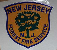 logo of New Jersey Forest Fire Service, featuring a blue shield in which is a green silhouette of a tree on a goldenrod yellow background with the works "New Jersey N.J. Forest Fire Service"