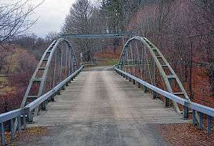 A metal bridge with two forked arches on the side and tie rods holding the middle together, seen from one end
