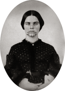 A black and white picture of a woman with a tattoo on her chin