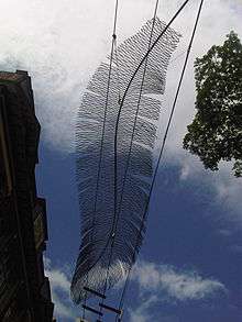 A wire sculpture shaped like a bird feather, silhouetted against the sky