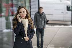 An image of a woman on a mobile phone with a man looking on
