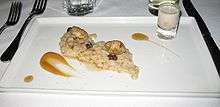 Two oysters and a handful of raisins rest atop a line of oatmeal. On either side is a streak of maple syrup. The dish is served on a white tray.