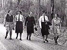 Five women in a mix of uniforms walking along a bush track