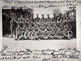 Group portrait of 38 men in military uniforms with peaked caps