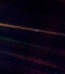 A tiny, pale blue dot is contrasted against the vastness of space