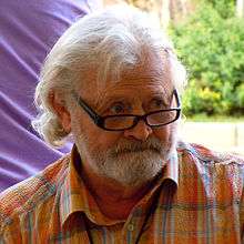 Portrait of male with white hair, white beard and spectacles wearing open-necked shirt