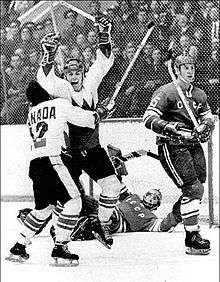 Henderson is embraced by teammate Cournoyer immediately following his winning goal. The Soviet goaltender lays prone in front of the net while another Soviet player skates away.