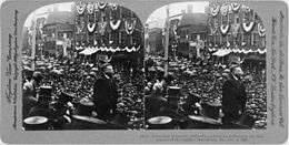 Two identical photos of a man looking out over a large crowd. The images are mounted side-by-side on a card.