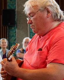 A white-haired man in a red T-shirt plays mandolin.