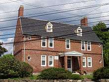 A 2+ story brick colonial house. The windows are comparatively narrow, and there are small round windows near the corners of.