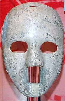 the mask is white and of solid construction with egg-sized oval cutouts for the eyes and a rectangular cutout from the base of the nose to below the lower lip
