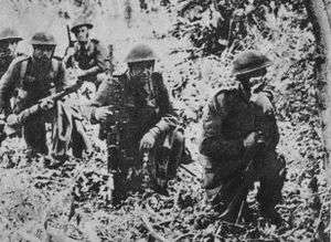 Five soldiers kneel down in woodland.