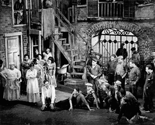 Black-and-white photo of a group of African American performers on a sparse stage in an urban setting.