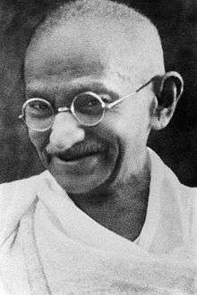 The face of Gandhi in old age—smiling, wearing glasses, and with a white sash over his right shoulder