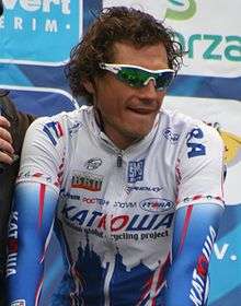 A road racing cyclist in a white and blue jersey with red trim, wearing sunglasses with white frames.