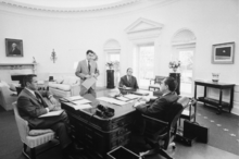  Richard Nixon sitting behind the Wilson desk with three chief advisers surrounding the desk.