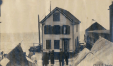 old photo showing a house being floated on small barges in the harbor