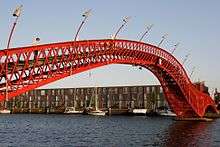 A red, twisting  bridge spans a canal.