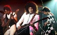 Colour photograph of John Deacon, Brian May and Freddie Mercury of Queen performing live in 1978.