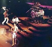 Colour photograph of all four members of Queen performing live in 1981.