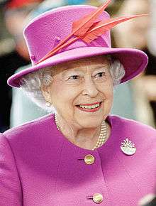 A smiling woman wearing a purple dress and matching hat.