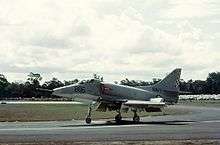 Colour photograph of a white military jet fighter taxiing along a runway