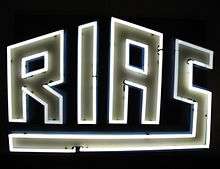 Stylized "RIAS" neon sign against black background