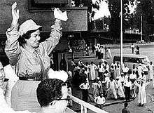 A woman in her thirties dressed in military garb waves to a crowd of supporters.
