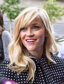 A smiling blonde-haired woman wearing polka dot black and white blouse