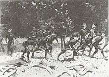Black and white print of an oil painting by Frederic Remington shows slouch-hatted soldiers advancing in a crouch while crossing a stream