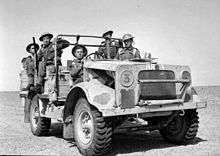 A military vehicle in the desert, with five soldiers aboard.