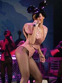 A woman wearing a high waisted pink sparkly outfit with large shoulder pads performing on a stage