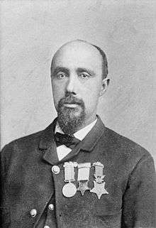 Head and shoulders of a balding black man with a goatee, wearing a suit coat, vest, and bow tie. On the jacket's left breast is a row of three medals.