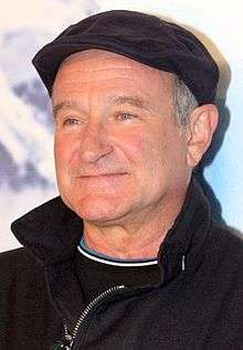 Robin Williams in a black coat looking towards his right and smiling