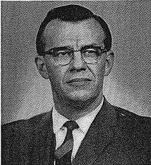 Black-and-white photograph of dark-haired man in suit and wearing glasses