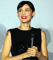 A smiling woman with short hair wears a black dress.