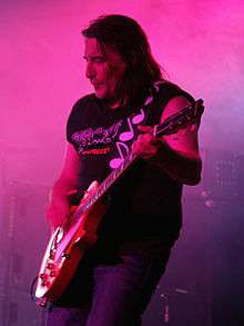 A man is shown in upper body profile from his left. He is playing an electric guitar.