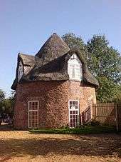 Two storey round thatched cottage with single doorway two windows on ground floor doorway sized and two thatched windows on the first floor