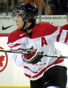 A hockey player in white and red uniform speed-skates across the ice, stick held at chest level.