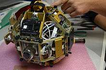 A SPHERES satellite without the plastic shell. Aluminum structure, a control panel, ultrasonic sensors, thrusters, pressure regulator knob and pressure gauge are visible.
