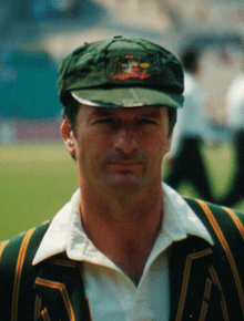 A white-skinned man posing in front of the camera; he is wearing a green cricket cap and shirt.